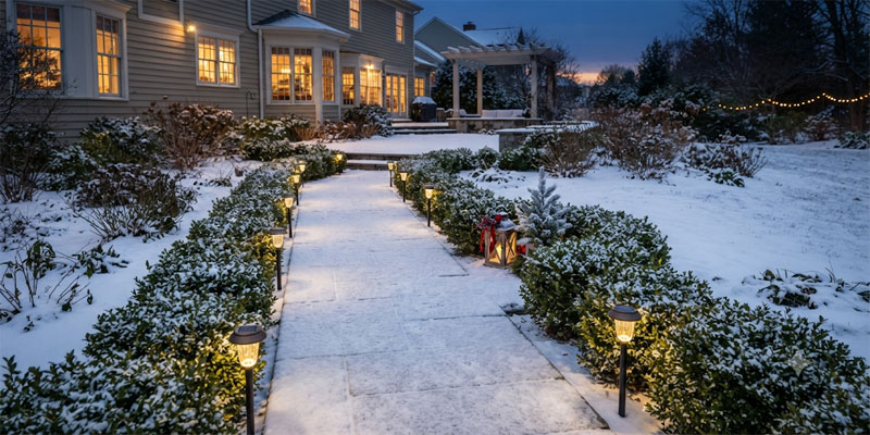 Eco-friendly solar Christmas lights illuminating a snowy garden pathway and red holiday accents
