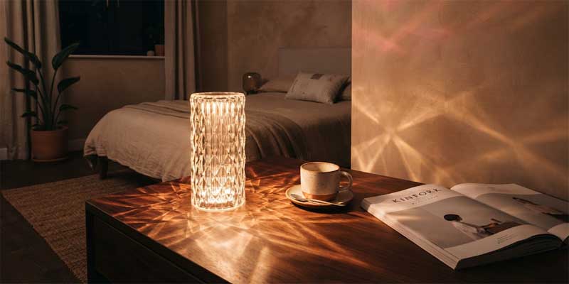 Modern cordless crystal lamp projecting radiant diamond rose light patterns across a wooden nightstand